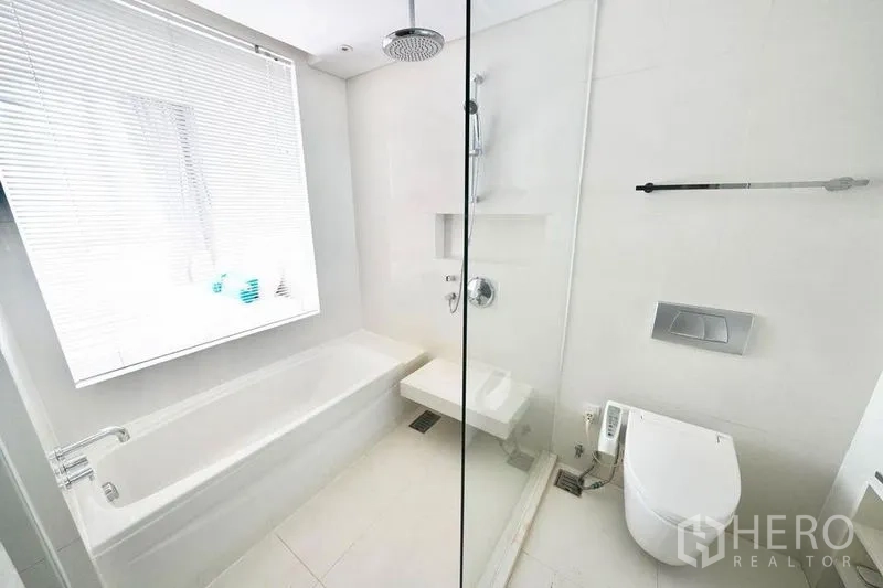 Condominium for rent or sale in Watthana, Bangkok - Bright white bathroom with bathtub, glass rain shower and modern bidet toilet in a Thonglor condo.