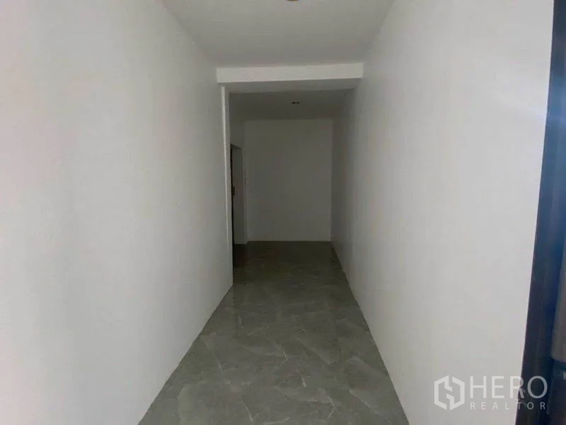 办公空间 出租在Watthana, Bangkok - 灰色地砖的狭长走廊，通向玻璃门办公室入口。