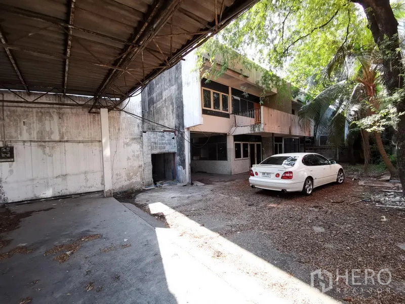 带办公室的家 出租在Khlong Toei, Bangkok - 前院可见停放的车辆、棚顶和两层建筑。