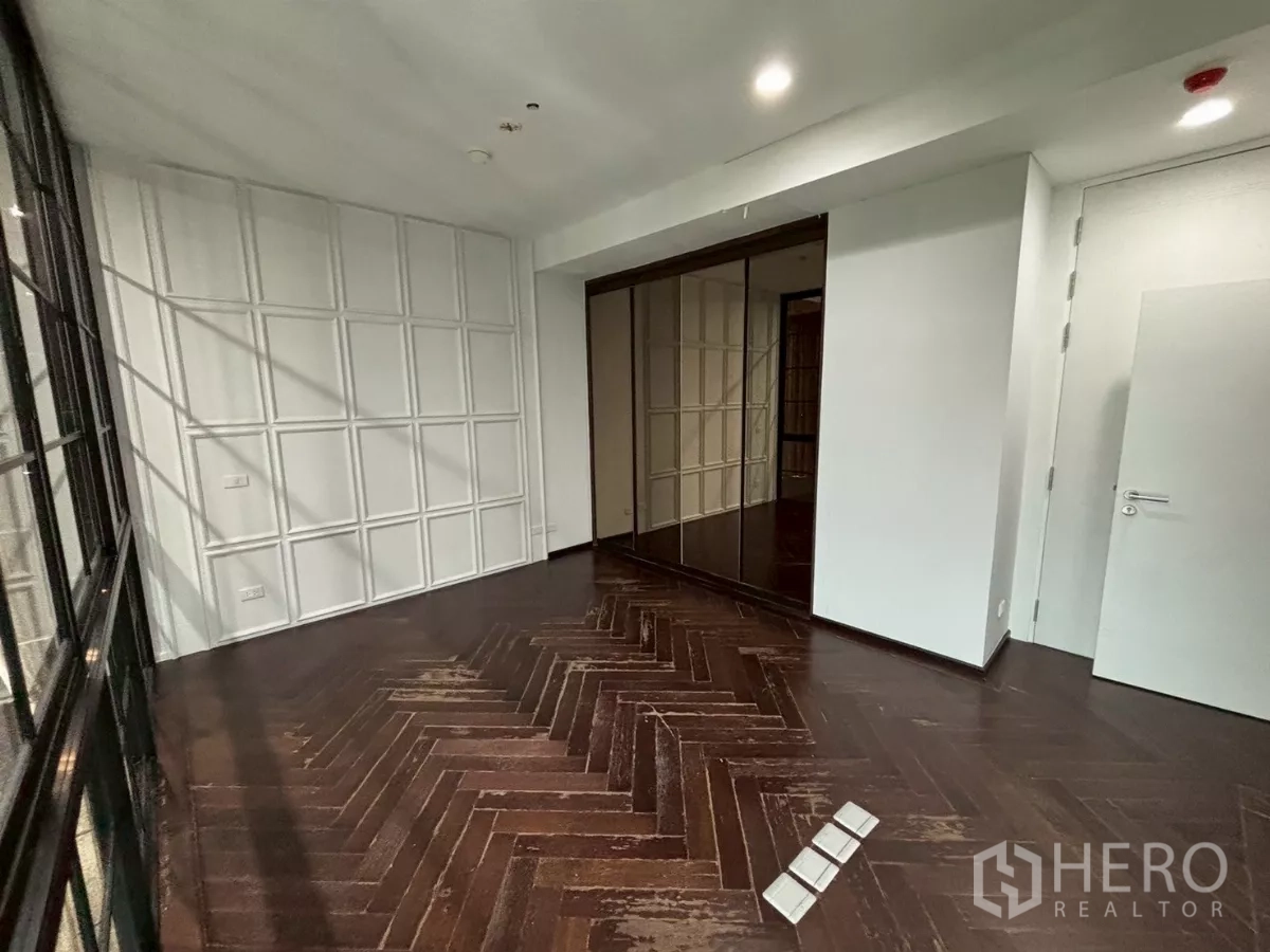 Condominium for sale in Bang Kho Laem, Bangkok - Bedroom with dark herringbone wood floor, mirrored wardrobe and a white paneled feature wall.