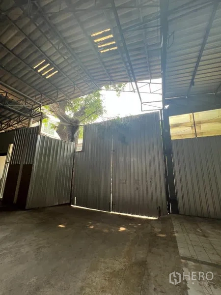 คลังสินค้า ให้เช่าในKhlong Toei, Bangkok - ประตูบานเลื่อนโลหะสูง แสงแดดส่องผ่าน เห็นต้นไม้นอกพื้นที่