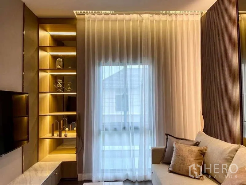 独立式住宅 出租在Bang Phli, Samut Prakan - 客厅一角，纱帘、内置灯光展示架与浅色沙发。