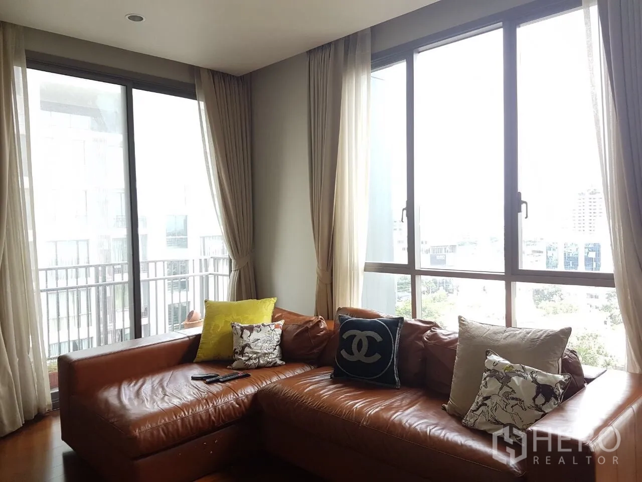 คอนโด ขายในWatthana, Bangkok - ห้องนั่งเล่นมุมห้อง โซฟาหนังตัวแอล หน้าต่างบานใหญ่ และวิวเมืองจากระเบียง