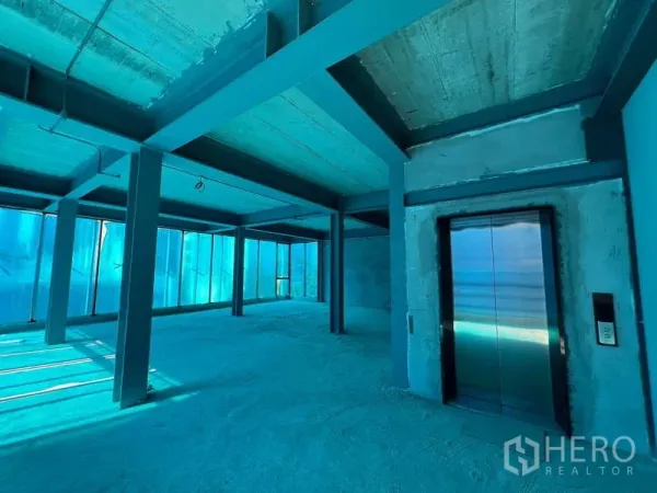 Retail Space for rent in Pathum Wan, Bangkok - Open-plan retail floor in shell condition with steel beams, concrete ceiling, floor-to-ceiling windows and a stainless elevator.