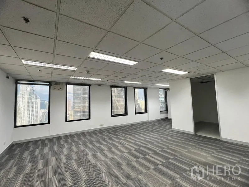 Office Space for rent in Khlong Toei, Bangkok - Open-plan office with grey carpet tiles, drop ceiling and skyline views through multiple windows.