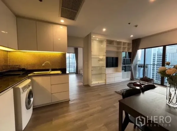 Condominium for rent in Bangkok - Open-plan kitchen with gold tile backsplash, washing machine and dining area facing floor-to-ceiling windows.