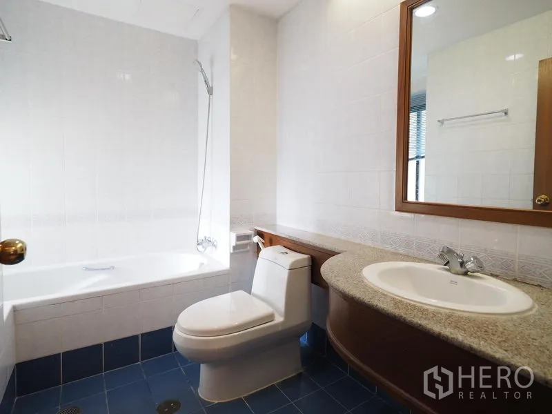 Condominium for rent in Sathon, Bangkok - Bathroom with bathtub and shower over tub, wide vanity, mirror and toilet in neutral tones.