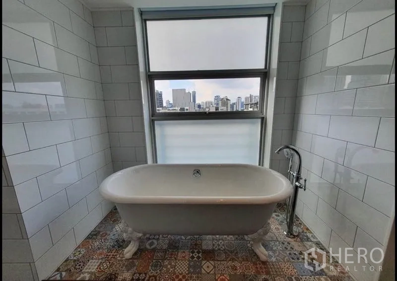 Condominium for rent in Watthana, Bangkok - Bathroom with freestanding clawfoot tub beside a window overlooking Bangkok skyline.