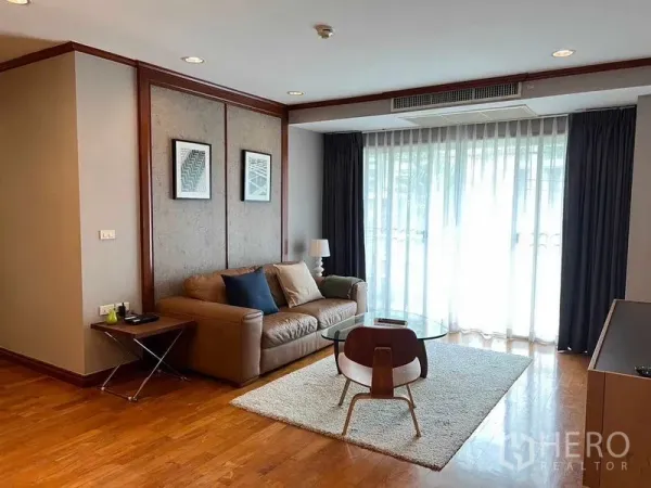 Condominium for rent or sale in Watthana, Bangkok - Living room angle showing sofa, lounge chair, rug, and sheer curtains letting in light