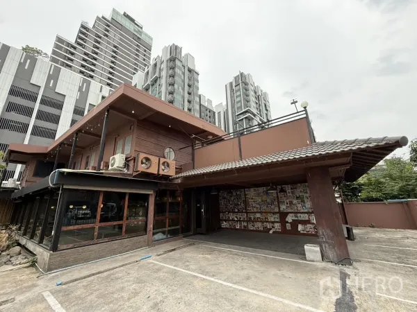 Detached House for rent in Watthana, Bangkok - Two-storey detached house with wood accents and covered parking, set against nearby high-rise buildings near Ekkamai.