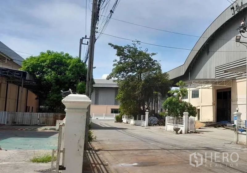 โรงงาน ให้เช่าในMueang Samut Prakan, Samut Prakan - ถนนทางเข้าแคมปัสโรงงาน มีต้นไม้ รั้วรักษาความปลอดภัย และพื้นที่จอดรถ