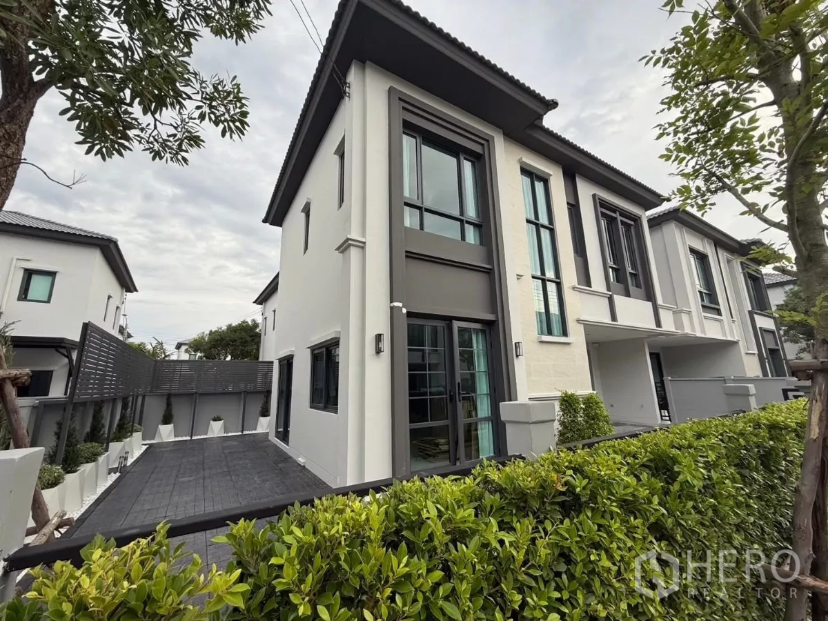 Detached House for rent in Bang Phli, Samut Prakan - Side exterior of the home showing tall windows, terrace and landscaped hedge.
