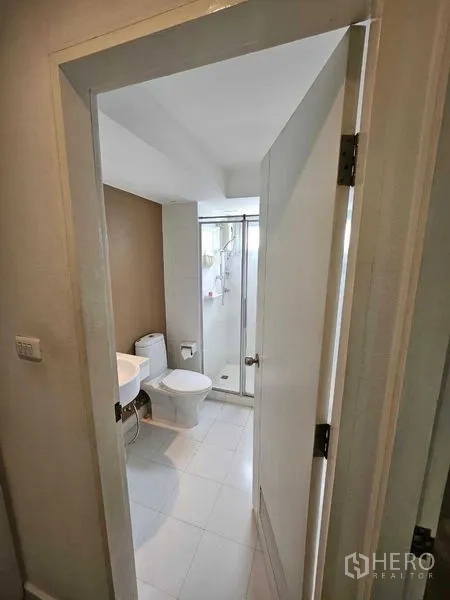 Condominium for sale in Watthana, Bangkok - Bathroom with glass-enclosed shower, toilet, and white tile flooring.