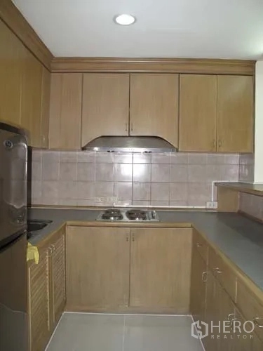 Condominium for rent in Sathon, Bangkok - Compact U-shaped kitchen with wooden cabinets, tiled backsplash, cooktop and range hood.