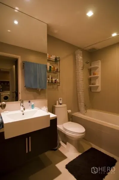 Condominium for rent in Khlong Toei, Bangkok - Modern bathroom with bathtub, vanity with large mirror, and toilet under recessed lighting.