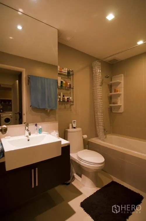 Condominium for rent in Khlong Toei, Bangkok - Modern bathroom with bathtub, vanity with large mirror, and toilet under recessed lighting.