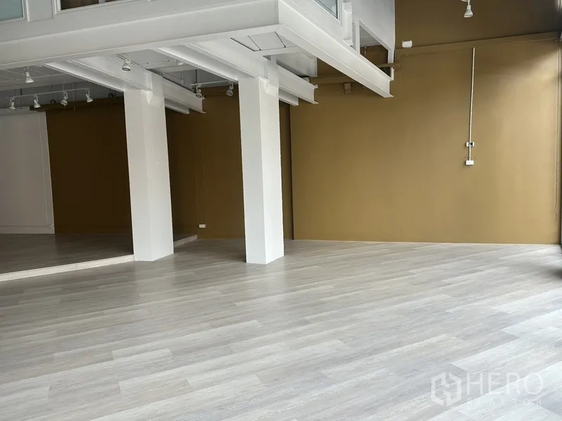 Retail Space for rent in Khlong Toei, Bangkok - Open retail zone with tan accent wall, white beams and light laminate flooring.