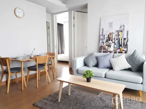 Condominium for rent in Khlong Toei, Bangkok - Bright living room with gray sofa, coffee table, dining table and doorway leading to the bedroom.