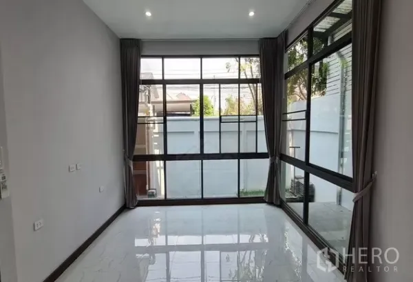 带办公室的家 出租在Watthana, Bangkok - 一层房间，转角落地大窗与灰色窗帘，面向小花园和围墙