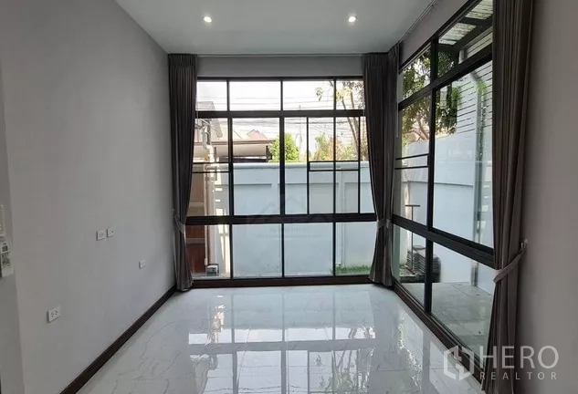 带办公室的家 出租在Watthana, Bangkok - 一层房间，转角落地大窗与灰色窗帘，面向小花园和围墙