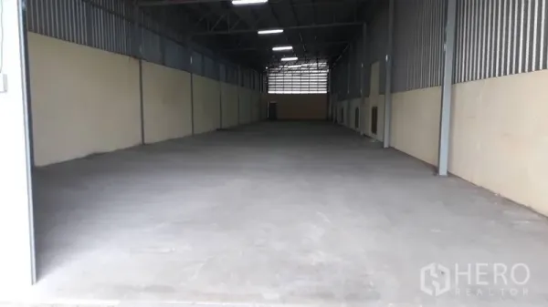Warehouse for rent in Mueang Nakhon Pathom, Nakhon Pathom - Long warehouse interior with high ceiling, bright lighting, and smooth concrete floor.