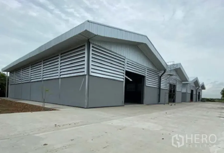 工厂 出租在Pathum Thani - 位于Lat Lum Kaeo的现代灰色钢结构工厂，山墙屋顶与百叶通风墙，前方为宽阔混凝土装卸场。