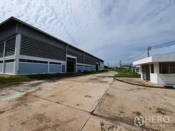 Factory for rent in Mueang Samut Prakan, Samut Prakan - Wide driveway with guardhouse and roller-shutter loading bay on the side of the factory building.