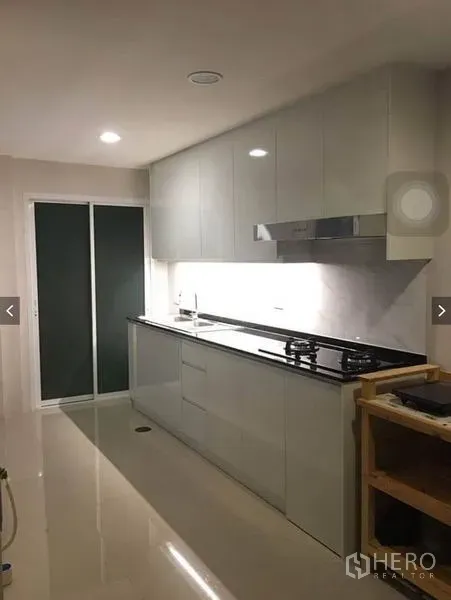 Townhouse for rent or sale in Suan Luang, Bangkok - Galley kitchen view showing sink, cooktop, overhead cabinets, and sliding door to the yard.