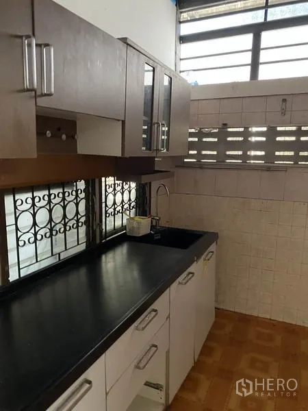 Townhouse for rent in Lat Phrao, Bangkok - Compact kitchen with upper and lower cabinets, black countertop, and barred windows.