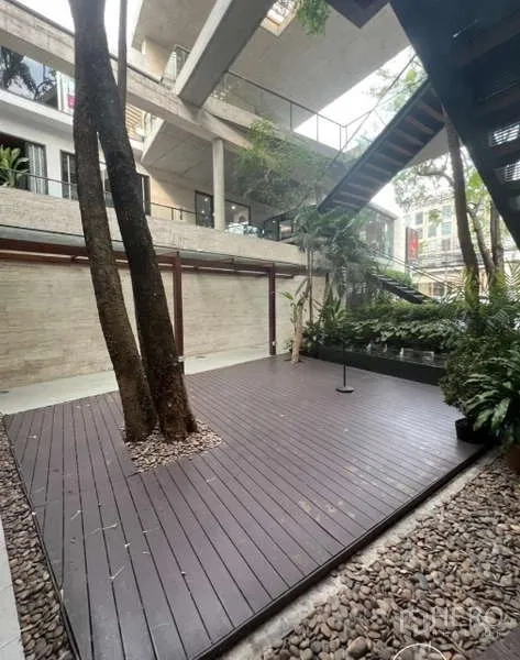 零售空间 出租在Watthana, Bangkok - 开放式中庭，木地台与大树并列，周围为混凝土步道。