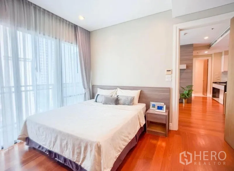 Condominium for rent in Khlong Toei, Bangkok - Primary bedroom with double bed, balcony-height windows and a bedside table.