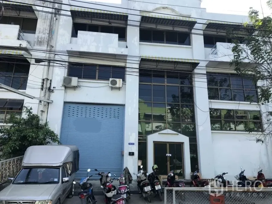 Factory for rent in Bang Sao Thong, Samut Prakan - Factory exterior with blue roller shutter, tall glass facade, and motorcycle parking.