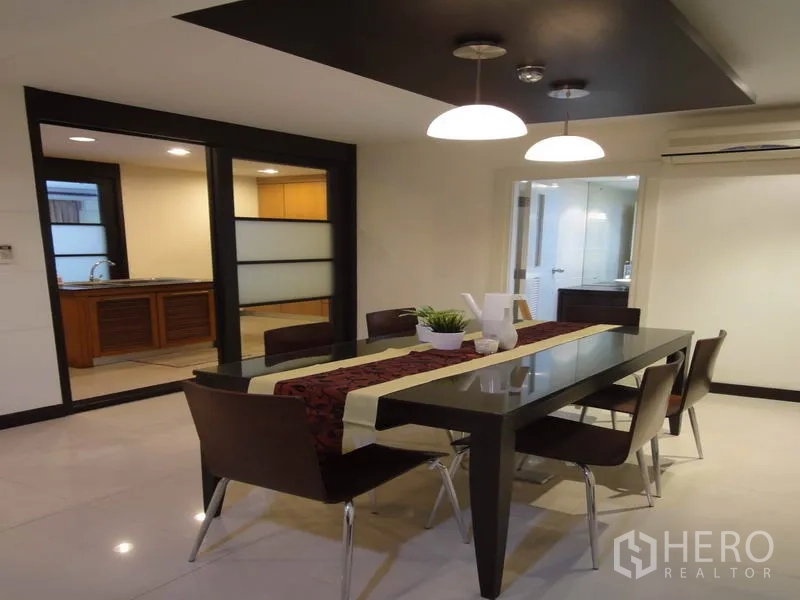 Condominium for rent in Watthana, Bangkok - Dining room with long table, pendant lights and access to the kitchen.