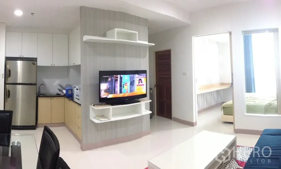 Condominium for rent in Phaya Thai, Bangkok - Open-plan living room with wall-mounted TV, L-shaped kitchenette and doorway to the bedroom in a modern Bangkok condo.