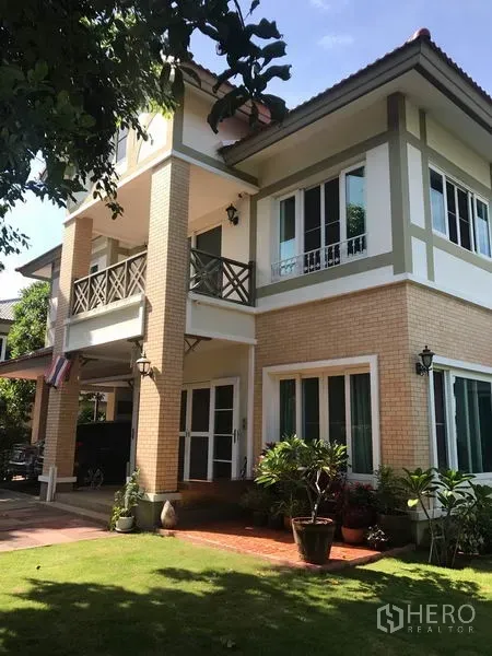 独立式住宅 出售在Pak Kret, Nonthaburi - 帕克烈两层独栋别墅外观，砖墙立面、阳台与修剪整齐的草坪。