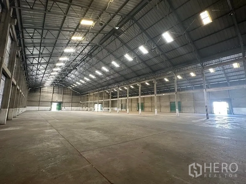Warehouse for rent in Mueang Pathum Thani, Pathum Thani - Large warehouse bay with several green sliding doors and drive‑through access.