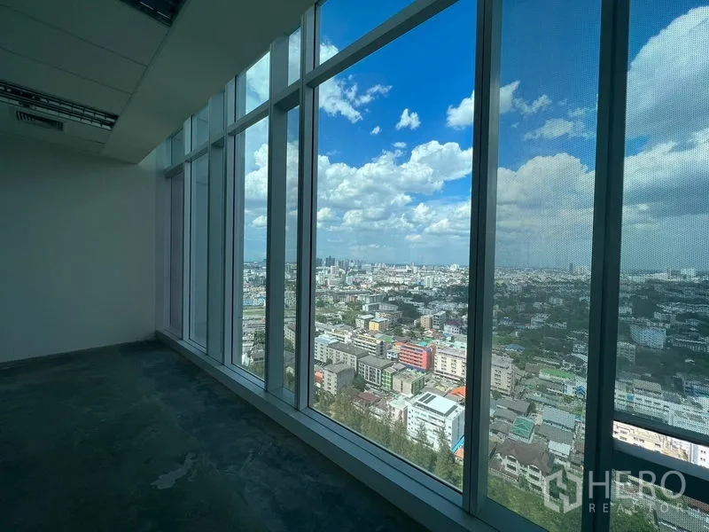 Office Space for rent - Panoramic city view through tall glass windows under a bright blue sky.