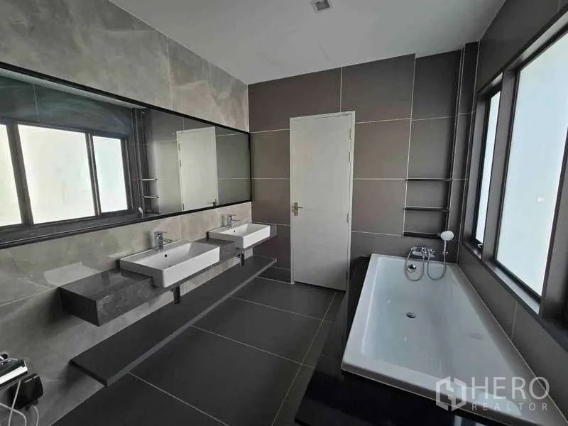 Detached House for rent in Bang Phli, Samut Prakan - Contemporary bathroom featuring twin basins, a long mirror and a bathtub beside windows.