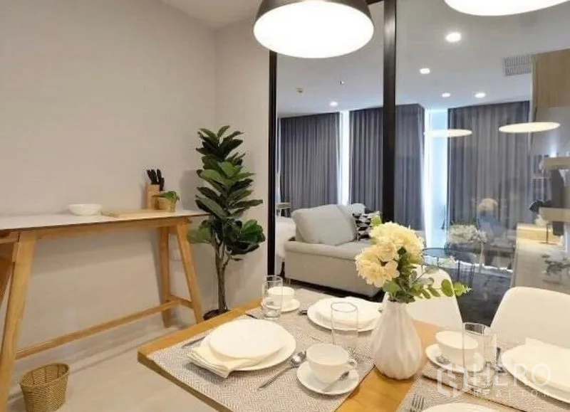 Condominium for rent in Pathum Wan, Bangkok - Dining table set for four looking toward the lounge with large windows and grey drapes.