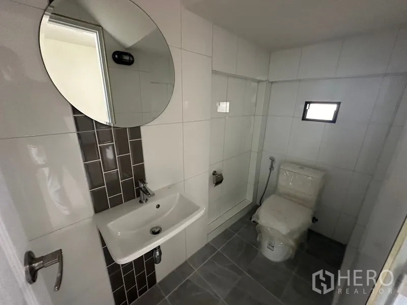 Home Office for rent in Wang Thonglang, Bangkok - Compact bathroom with round mirror, white tiles, and a walk-in shower.