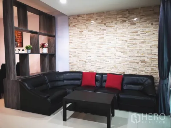 Townhouse for rent in Suan Luang, Bangkok - Cozy living area with black L-shaped leather sofa and stone accent wall.