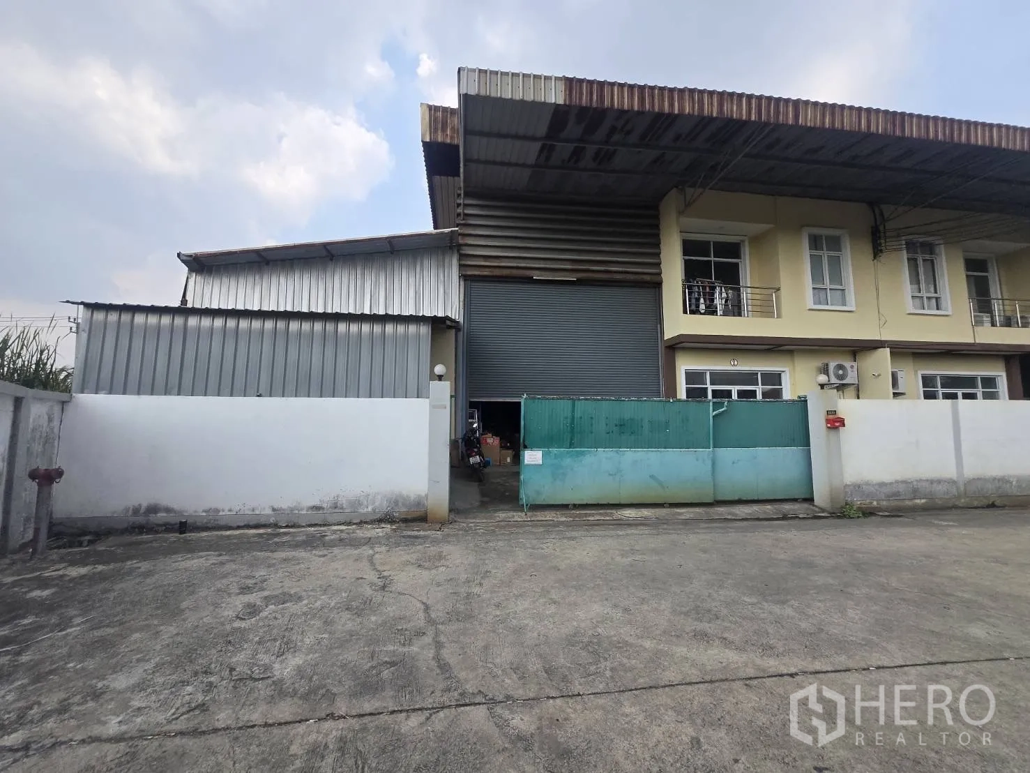 โรงงาน for rent or sale in Mueang Samut Sakhon, Samut Sakhon - ด้านหน้าโรงงานมีประตูม้วนขนาดใหญ่ รั้วและลานจอดรถ