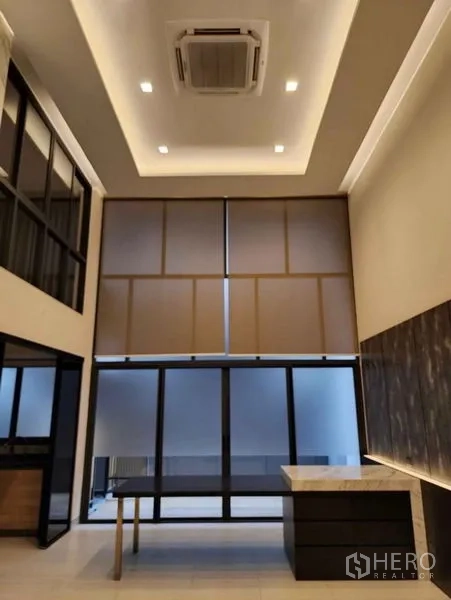 Townhouse for sale in Yan Nawa, Bangkok - Open-plan living room with tray ceiling, cassette air conditioner and floor-to-ceiling windows with shades.