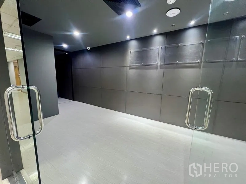 办公空间 出租在Watthana, Bangkok - 玻璃双开门入口，现代办公室前厅，深色特色墙与射灯。