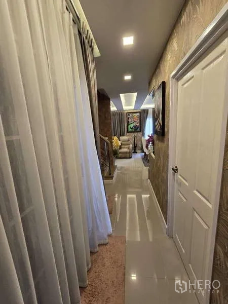 Detached House for rent in Thanyaburi, Pathum Thani - Hallway view toward the lounge and staircase with warm cove lighting.