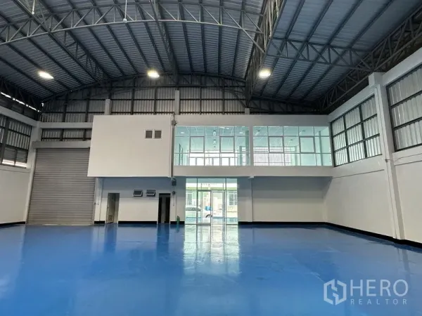 Factory for rent in Khlong Luang, Pathum Thani - Warehouse interior showing a roller shutter loading door and mezzanine glass office overlooking the floor.