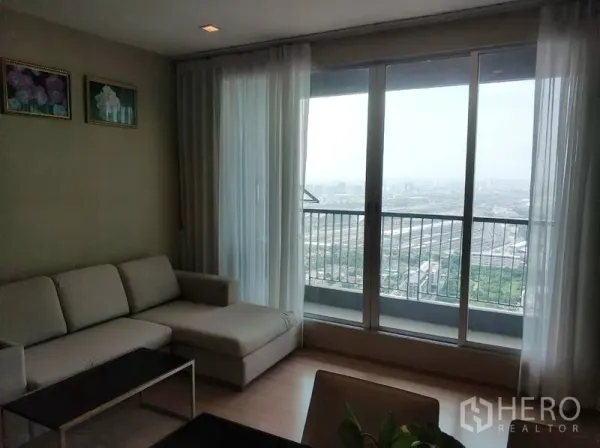 คอนโด ให้เช่าในPhaya Thai, Bangkok - ห้องนั่งเล่นโซฟา L เชื่อมระเบียงด้วยประตูกระจกเต็มบาน มองเห็นวิวสกายไลน์