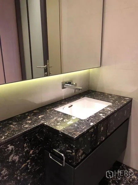 Condominium for rent in Khlong Toei, Bangkok - Contemporary bathroom with black marble vanity, under-cabinet lighting, and wall-mounted faucet.
