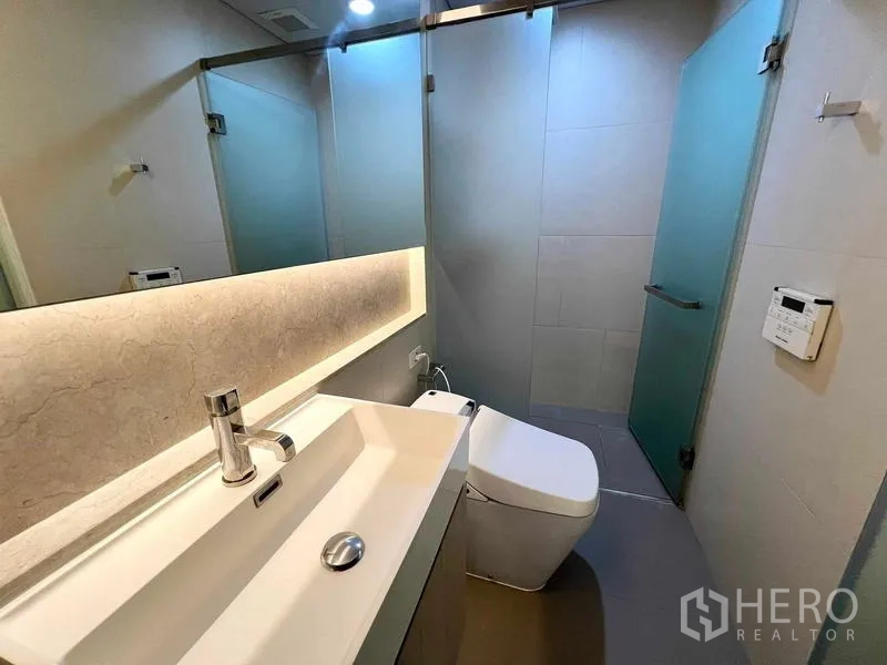 Condominium for rent or sale - Bathroom with long countertop sink, glass-enclosed shower, and backlit mirror.