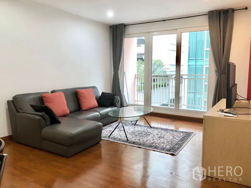 公寓 出租或出售在Watthana, Bangkok - 客厅配L形皮沙发、玻璃咖啡桌与地毯，落地窗通向阳台